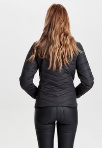 Czarna pikowana kurtka o dopasowanym kroju, z wysokim kołnierzem i długimi rękawami. Noszona z czarnymi, teksturowanymi spodniami. Gładkie wykończenie materiału.