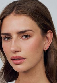 Guldringar med en vågig design, visade mot en modells neutrala bakgrund, vilket framhäver deras blanka, reflekterande textur.