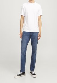 Camiseta de algodón blanca con mangas cortas, combinada con unos vaqueros de mezclilla azul oscuro. Zapatillas bajas en blanco y negro con cordones.