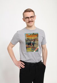 Šedé bavlněné tričko s barevným grafickým motivem skateboardového magazínu na přední straně. Klasický kulatý výstřih a uvolněný střih.