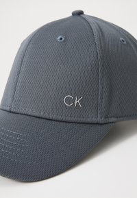 Grijze mesh honkbalpet met een gebogen rand, met een subtiele "CK" logo in zilver. Inclusief ventilatiegaten bovenop.