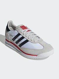 Heren sportschoenen met een witte stoffen bovenkant, grijze suède accenten, drie zwarte strepen, rode details en een gestructureerde rubberen zool.