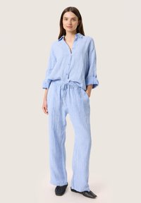 Ljust blå randig loungewear-set med en knappad skjorta med uppvikta ärmar och byxor med elastisk midja. Mjuk, andningsbar tyg.