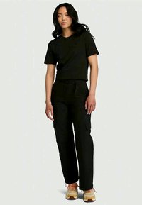 T-shirt preto crop emparelhado com calças cargo largas pretas. O conjunto apresenta vários bolsos e é complementado por sapatos de cor clara.