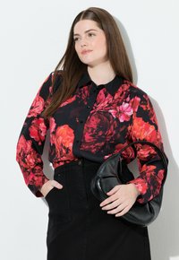 Bloemige overhem-shirt met rode en roze bloemen op een zwarte achtergrond; gecombineerd met een zwarte leren handtas en een zwarte rok met zakken.