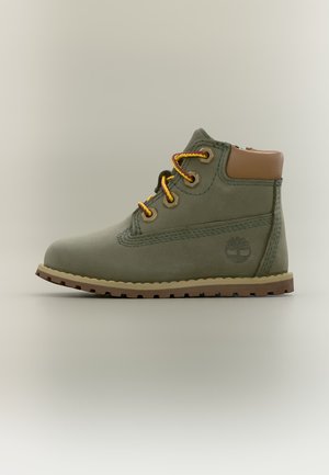 Olivgrüner Knöchelstiefel mit braun gepolstertem Kragen, gelben und braunen Schnürsenkeln, robuster Sohle und eingeprägtem Baum-Logo an der Seite.