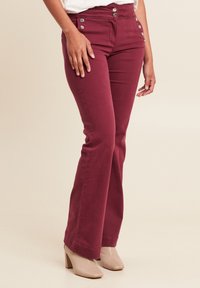 Burgundy flared jeans met een hoge taille, voorzien van twee zilveren knoopaccenten en voorzakken. Zachte stof met een gladde textuur.