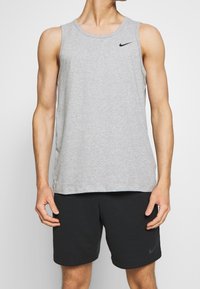 Šedý sportovní tílko vyrobené z bavlněné směsi, s kulatým výstřihem a malým černým logem Nike na hrudi.