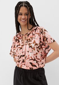 Kurzarmige, locker sitzende Bluse aus sanftem rosa Stoff mit abstrakten braunen und cremefarbenen Mustern; verfügt über ein Keyhole-Ausschnitt-Detail.