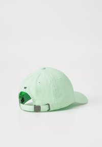 Lys grøn bomulds baseball cap med en buet skygge og justerbar metalspænde bagpå; har ventilationshuller og mindre syningsdetaljer.