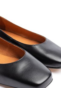 Paire de chaussures plates en cuir noir avec bouts carrés arrondis et doublure intérieure marron, vue en gros plan sur fond blanc.