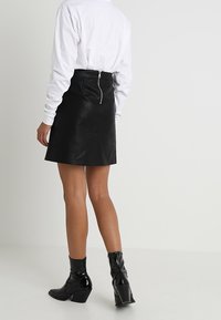 Mini gonna in pelle nera con silhouette aderente, dotata di una chiusura zip metallica visibile sul retro e una texture liscia e lucida.