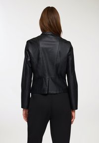 Giacca di pelle nera con un design aderente, colletto a fazzoletto e dettagli con cuciture centrali sul retro. La giacca ha un orlo cropped e maniche lunghe.