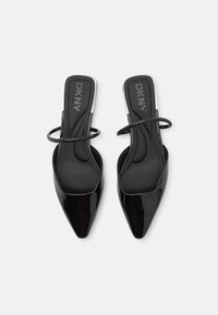 Zwarte gepatineerde leren slingback hakken met een puntige neus, voorzien van een dunne enkelband en een zwarte, gestructureerde binnenzool. DKNY-logo zichtbaar.