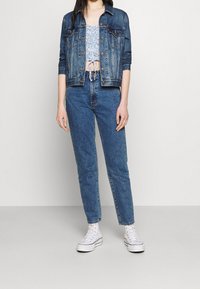 Chaqueta de mezclilla de color azul desgastado, de mangas largas, con cierre de botones, top elástico corto, jeans ajustados de tiro alto en azul y zapatillas altas blancas.