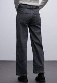 Vaqueros de pierna ancha gris oscuro, fabricados en denim, con un diseño de cinco bolsillos, yugo trasero y costuras discretas en los bolsillos traseros.