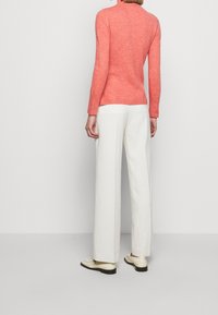 Maglione a maglia corallo con colletto alto, abbinato a pantaloni bianchi a gamba larga e scarpe color crema. Texture liscia e design aderente in vita.