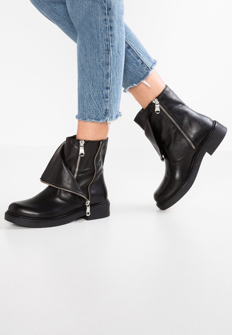 Czarne skórzane botki na kostkę z bocznym zamkiem, charakteryzujące się złożonym designem i strukturalnym wykończeniem. Gładka czarna gumowa podeszwa, minimalne akcenty.
