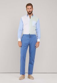 Camicia da uomo a blocchi di colore in verde chiaro e blu con taschino sul petto; abbinata a pantaloni blu. Tessuto morbido. Calzature casual completano il look.
