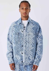 Chaqueta vaquera de lavado claro con un patrón pixelado en diferentes tonos de azul, con cierre frontal de botones y dos bolsillos en el pecho.