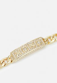 Zlata zapestnica s središnjim ploščkom, okrašenim s prozornimi kristali in gravuro "XOXO", s gladko in sijočo površino.