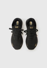 Μαύρα αθλητικά παπούτσια με υφασμάτινο επάνω μέρος με υφή, κλείσιμο με κορδόνια, χρυσές λεπτομέρειες και πάτους με μαξιλάρι, με αεροδυναμικό σχέδιο.