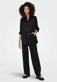 Camicia nera a maniche lunghe con chiusura a bottoni, abbinata a pantaloni larghi coordinati, entrambi realizzati in tessuto morbido e con una vestibilità rilassata.