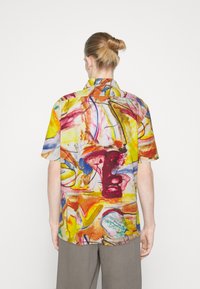 Cămașă cu mânecă scurtă dintr-un material ușor, având un imprimeu abstract cu nuanțe vibrante de galben, roșu și albastru, și o croială relaxată.