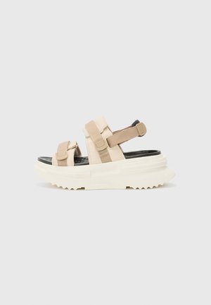 Beige platform sandals with adjustable straps, black insole, and textured white outsole. Features a chunky sole and sturdy design.