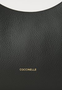 Black textured leather handbag with a rounded top, featuring a subtle gold "Coccinelle" logo embossed on the front.