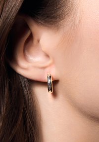 Złote kolczyki w formie obręczy o teksturowanej powierzchni, z polerowanym wykończeniem. Posiadają okrągły kształt, dopasowując się ściśle do płatka ucha.