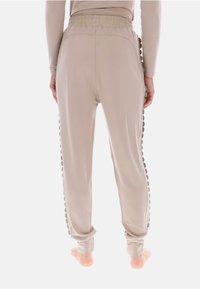 Beżowe spodnie do noszenia w domu z elastycznym pasem i ozdobnymi okrągłymi elementami wzdłuż bocznych szwów. Wykonane z miękkiego, rozciągliwego materiału.