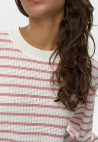 Kötött pulóver vízszintes rózsaszín és fehér csíkokkal, bordás nyakkal és texturált anyaggal. Közelről a felső rész.