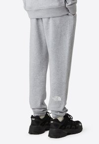 Grå joggebukser laget av mykt stoff, med elastiske mansjetter og sidelommer. Vist sammen med svarte treningssko med synlig merkevarelogo.