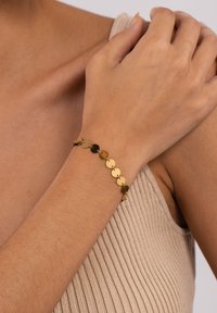 Goldfarbener Armreif mit runden, polierten Scheiben, die durch kleine Glieder verbunden sind. Wird am Handgelenk getragen und zeigt ein minimalistisches Design.