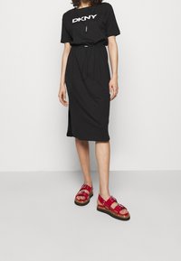 Svart midiklänning med samlad midja och sidoklyfta; kombinerad med röda sandaler med spänne och kraftig sula.