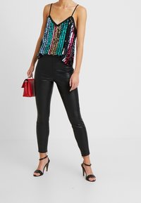 Svart paljettcamisole med färgglada vertikala ränder, kombinerad med åtsittande svarta byxor i konstläder och svarta klacksandaler. Röd handväska.