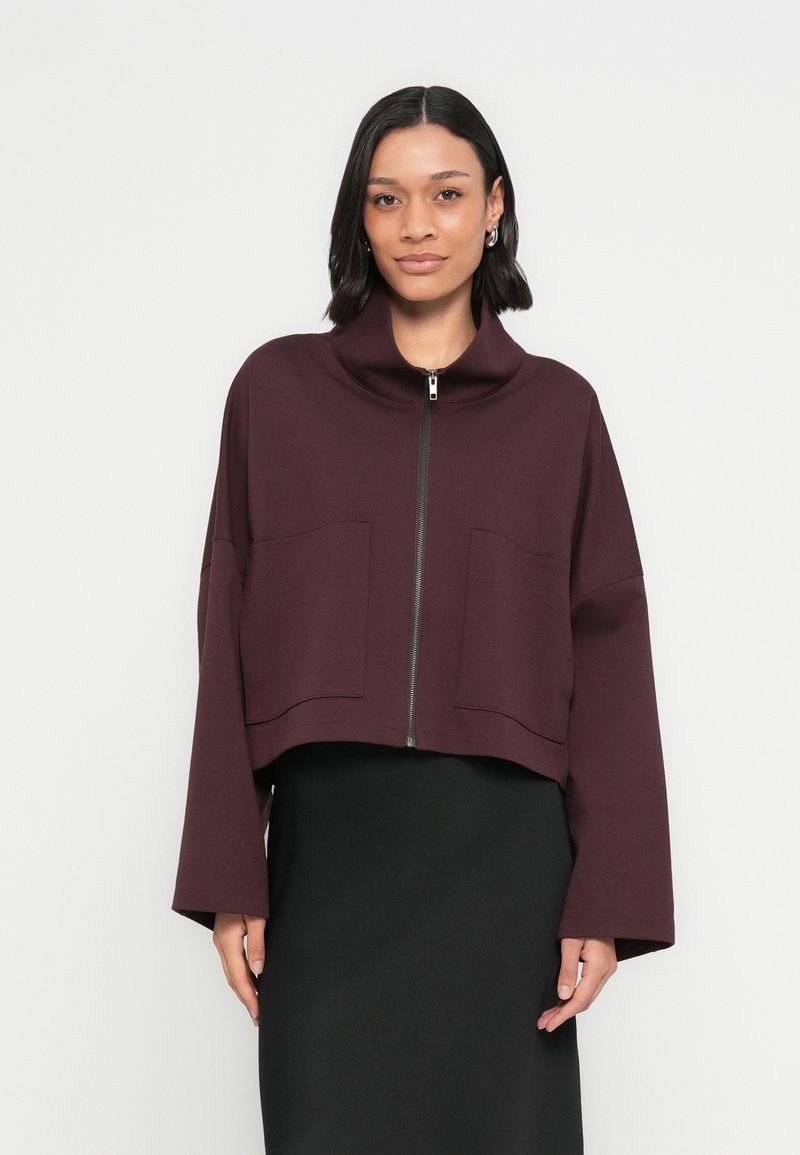 Bordowa krótka kurtka z wysokim kołnierzem, zamkiem z przodu i dwoma dużymi kieszeniami z przodu. Miękki, g�ładki materiał, luźny krój i szerokie rękawy.