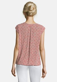 Blusa a maniche corte in corallo con motivo geometrico, caratterizzata da una cucitura centrale sul retro. Realizzata in tessuto leggero e fluido.