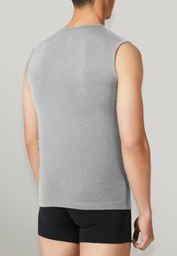 Maglietta grigia senza maniche realizzata in tessuto morbido, con scollatura rotonda e una vestibilità rilassata. Indossata con pantaloni boxer neri.