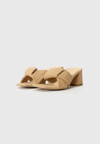 Sandale cu toc din suede bej, cu un design cu bretele încrucișate, vârful deschis și toc pătrat. Textura este moale, iar forma este modernă.