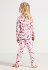 Rosa Schlafanzug-Set mit langen Ärmeln und Hose, versehen mit festlichen Mustern von Ornamenten, Bändern und Sternen. Hergestellt aus weichem Stoff.