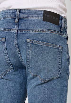Jeans in denim blu con un design a vita media, due tasche posteriori con dettagli cuciti e un'etichetta nera sul cinturino.