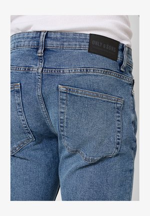 Jeans de mezclilla azul con un diseño de tiro medio, dos bolsillos traseros con costuras decorativas y una etiqueta negra en la cinturilla.