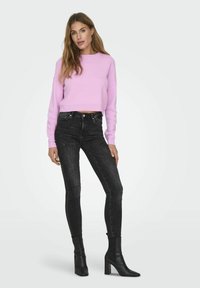 Pull court rose à manches longues, associé à un jean skinny noir et des bottes à talons blocs noires. Design épuré avec des accents minimalistes.