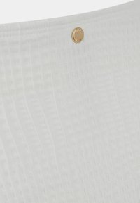 Tessuto bianco con un motivo testurizzato e sottili scanalature, accentuato da un piccolo bottone con logo dorato. Superficie liscia con una finitura pulita.