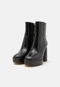 Bottes noires en cuir à la cheville avec une finition brillante, présentant un talon haut en bloc, une fermeture éclair et des détails en argent sur le côté.