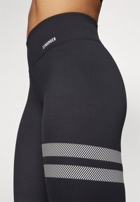 Black leggings with a smooth texture, featuring white "STRONGER" text at the waist and white striped pattern near the lower leg.