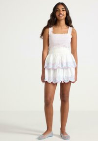 Abito bianco a strati con orlo scalloppato ricamato in rosa e blu, dotato di corpo smock e spalline regolabili. Abbinato a scarpe in rete.