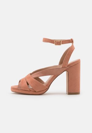 Pink damesandal i ruskind med høj hæl, åben tå, krydsede stropper, ankelrem med guldbærlås og blokhæl.